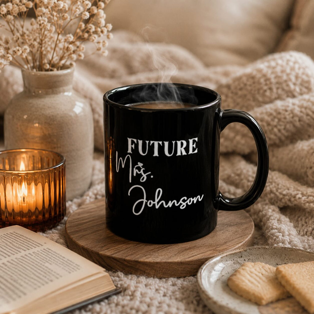 Future Mrs. black mug personalized with surname, styled with book, candle, dried flowers, and cookies