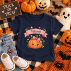 Toddler wearing personalized pink pumpkin Halloween t-shirt at a pumpkin patch